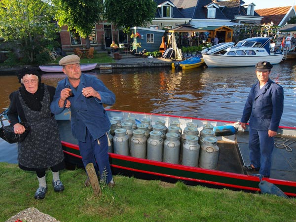 Hedendaags Warten en de reporter van Friesland Holland’s nieuwsdienst jagen Sytze en Maaike de stuipen op het lijf. Ze hebben zich teruggetrokken in het diorama van ‘It Earmhûs’ van museum ‘De Súdwâl’ in Warten, nu hun thuis na een kluizenaarsbestaan in het veenmoeras. Rechts “melkvaarder” Pieter Postma.